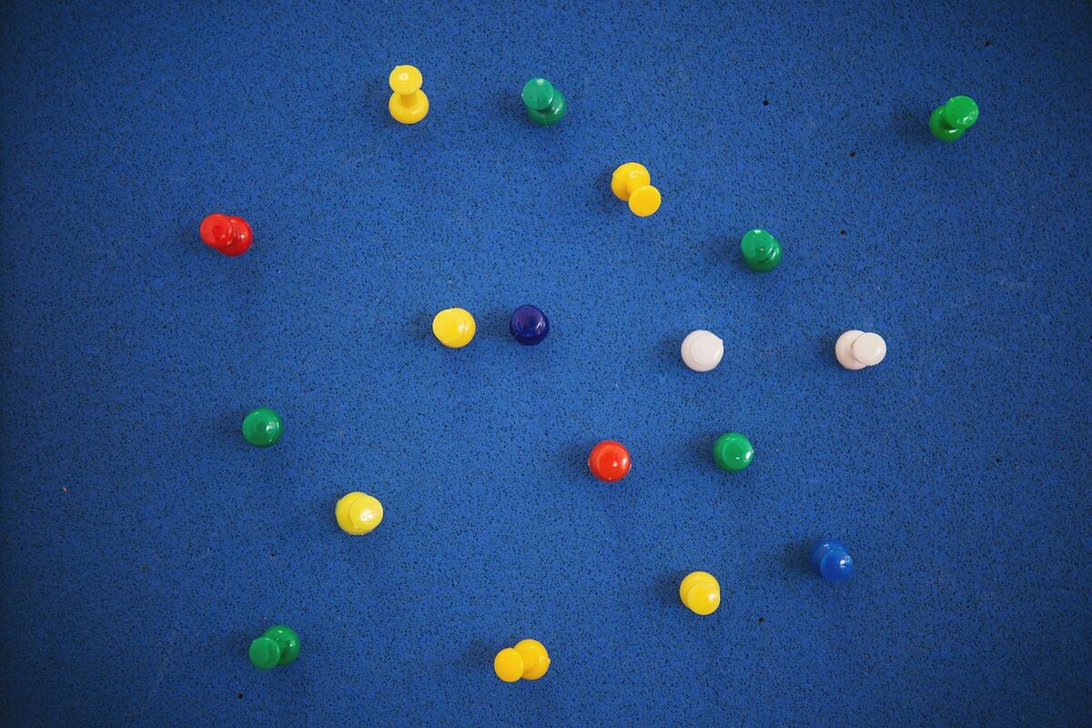 Colorful push pins in red, yellow, green, blue and white scattered across a blue cork board